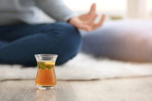 Cup,Of,Hot,Tea,And,Woman,Meditating,On,Floor,At